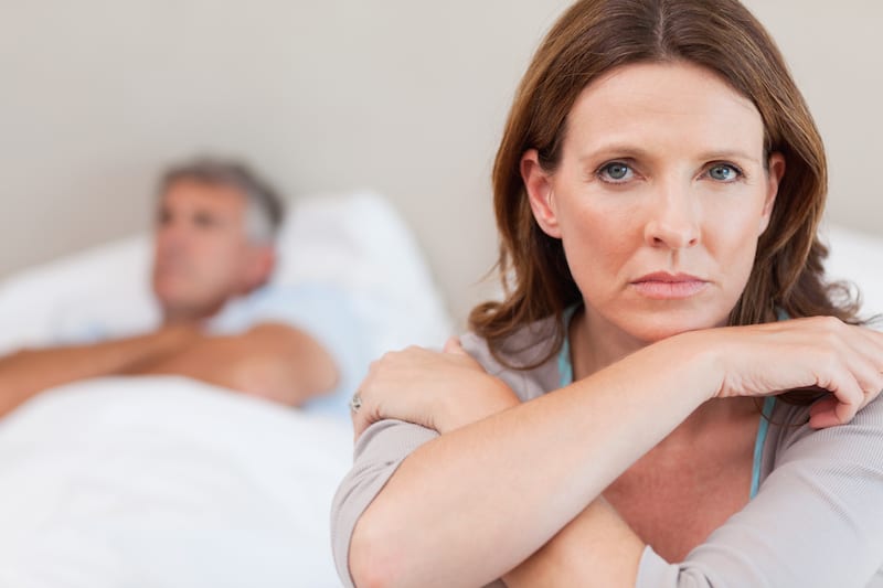 Woman suffering menopausal depression and anger with husband who's asleep in bed