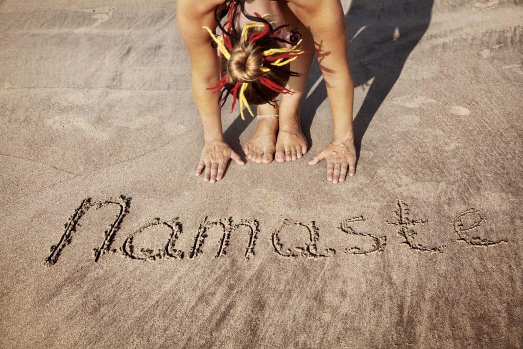 Woman doing yoga on the beach with the word namaste written in the sand at her feet